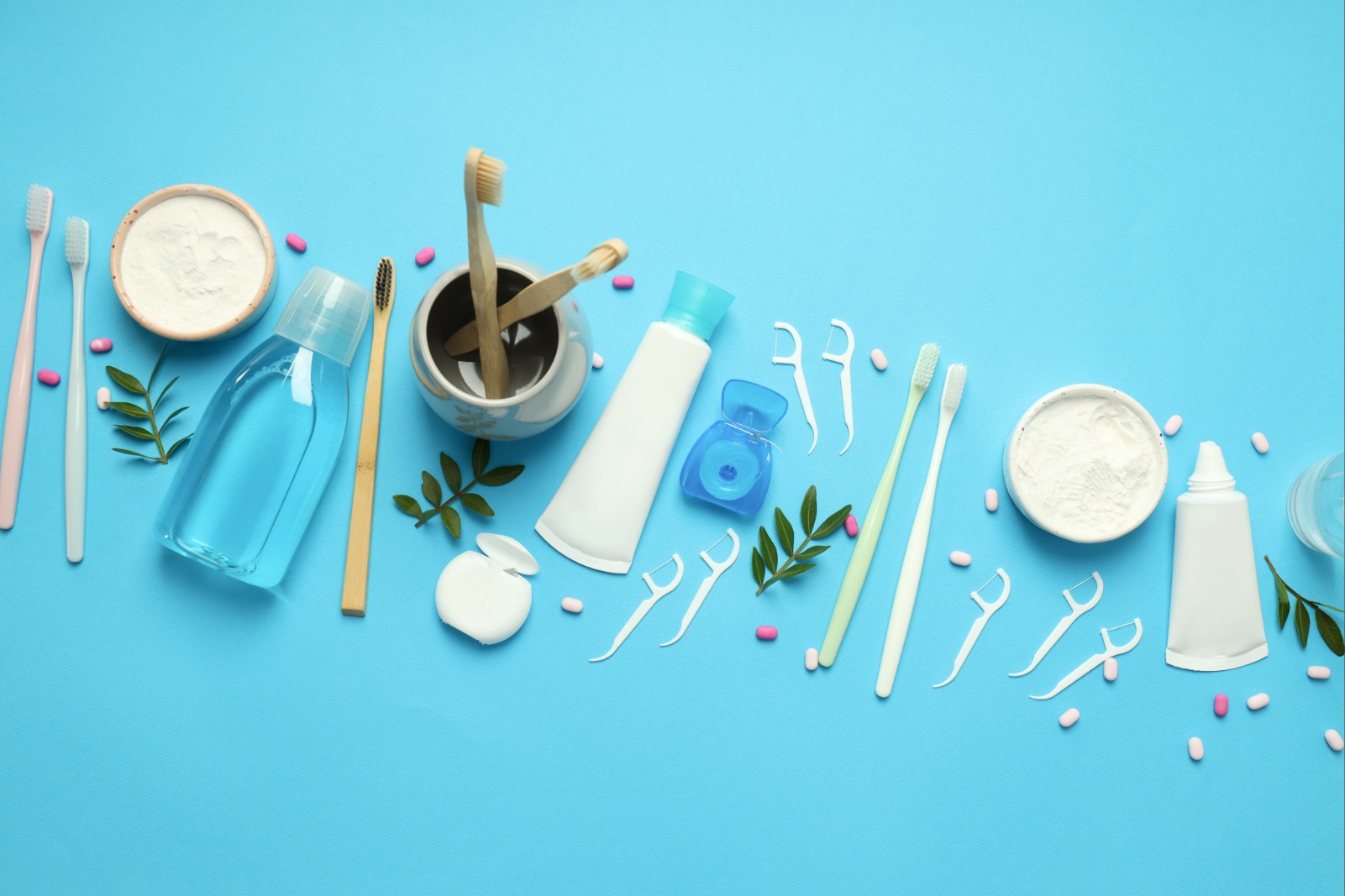 Verschiedene Mundhygiene-Produkte wie Zahnbürsten, Zahnseide, Zahnpasta und Mundspülung auf blauem Hintergrund für die tägliche Zahnpflege.